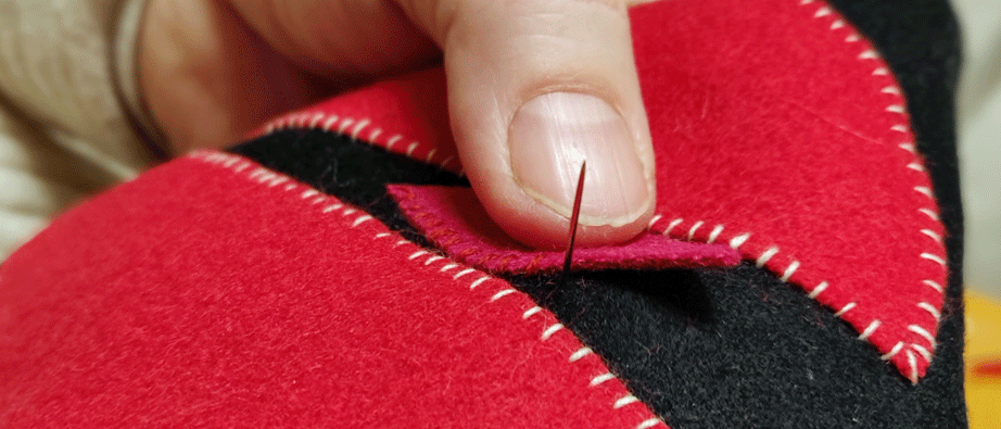 En persons hand syr med en nål och tråd i ett rött ylletyg.